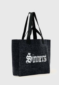 Czarna filcowa torba na ramię z dwoma czarnymi paskami z tkaniny. Na jednej stronie znajduje się biały napis „Sinners” w pogrubionej, stylizowanej czcionce.