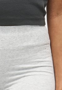 Gros plan d'une personne portant un haut côtelé gris foncé et un pantalon ajusté gris clair, montrant la taille et le côté du bras.