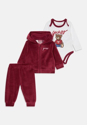 Completo per bebè in velluto rosso che include una felpa con zip, pantaloni coordinati e un body bianco con una grafica di orso e il testo "Guess".