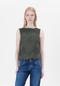 Olivengrønn strikket ermeløs topp med blomsterdesign og en teksturert, åpen vev. Kombinert med blå denimjeans.
