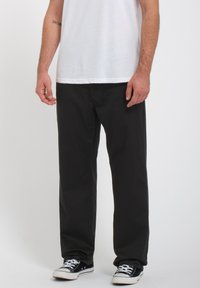 Pantalones de algodón negros con un corte relajado, que presentan una textura suave y un diseño de pierna recta, combinados con una camiseta blanca lisa y zapatillas negras.