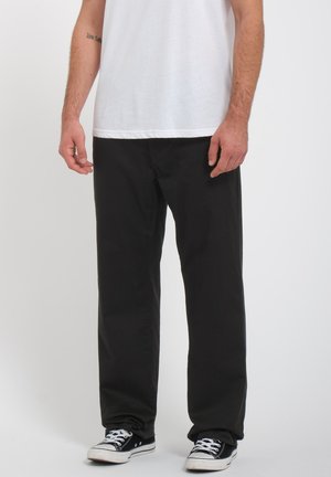 Black cotton trousers with a relaxed fit, featuring a smooth texture and straight leg design, paired with a plain white t-shirt and black sneakers.