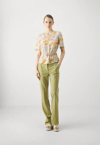 Blouse à motifs floraux dans des couleurs pastel avec une taille peplum, complétée par un pantalon vert taille haute et des sandales beiges.