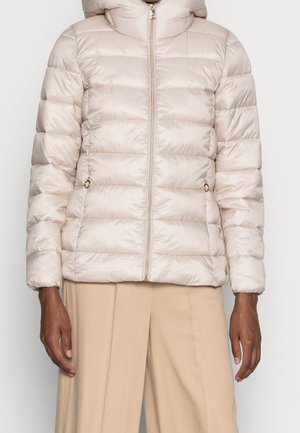 Lichtbeige doorgestikte pufferjas met ritssluiting aan de voorkant en met rits sluitbare zijzakken, gedragen met beige wijduitlopende broek.