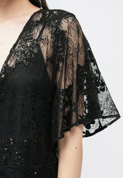 Juoda nėriniuota suknelė su trumpomis, išmatuotomis rankovėmis, papuošta blizgučiais ir gėlių raštu, išryškinanti tekstūruotą paviršių.