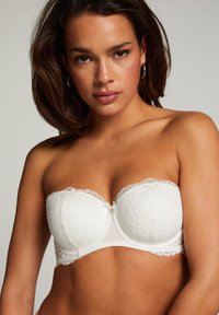 Witte strapless bh in bloemenkant met een gladde band, voorzien van een delicate kantafwerking en een klein strikje in het midden voor.