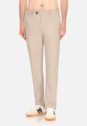 Pantalones beige de corte recto, que presentan un único botón frontal, trabillas para cinturón y una textura suave, combinados con zapatillas en blanco y negro.