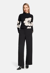 Czarny sweter z dużym białym wzorem kwiatowym, okrągły dekolt, długie rękawy, zestawiony z czarnymi spodniami w wysokim stanie i botkami.