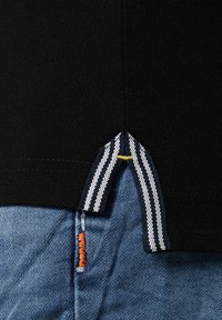Black garment with horizontal texture, featuring a striped accent at the hem. Below, blue denim trousers with a visible orange stitch detail.