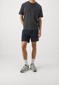 Dark gray cotton t-shirt with a chest pocket, paired with navy shorts, white ankle socks, and gray sneakers with black and green accents.
