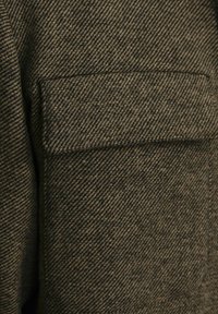 Ruskea herringbone-kuosisella kankaalla, jossa on litteä tasku. Tekstuurin pinta vaikuttaa eheyltä ja hieman karhealta, ja siinä on jäsennelty muotoilu.