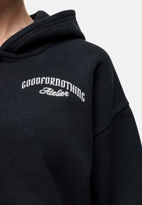 Felpa nera con cappuccio caratterizzata da testo ricamato bianco "GOODFORNOTHING Atelier" sul petto, con una texture morbida e una vestibilità comoda.