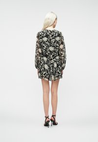 Abito mini nero a fiori con maniche lunghe trasparenti e gonna plissettata. Caratterizzato da un collo tondo e tessuto leggero e strutturato.