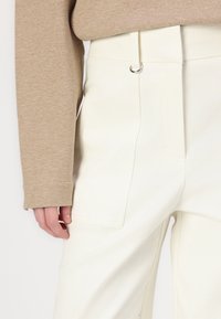 Witte, hooggewaiste broeken met zijzakken en een strak ontwerp. Geverfd met een textuur beige lange mouw top. Zilveren accenten zichtbaar.