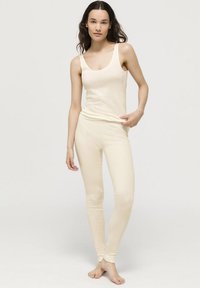 Krémový top na ramínka a legíny vyrobené z měkké látky; top má široká ramínka, legíny mají přiléhavý střih s žebrovanými lemy.