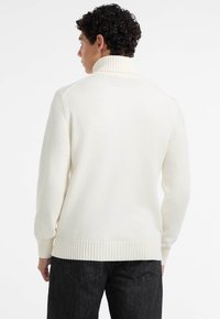 Maglione in cotone avorio con colletto a coste alto, maniche lunghe e orlo a coste. Presenta un tessuto texture e una vestibilità relaxed.