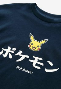 Námořnická modrá mikina s grafickým motivem Pikachu nad textem "ポケモン" a "pokémon". Materiál vypadá měkký a má kulatý výstřih.