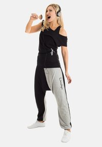 Black and gray sporty outfit featuring an off-shoulder black top and loose gray pants, adorned with a white logo, worn with headphones.