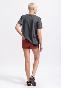 Grijze t-shirt met korte mouwen in een ontspannen pasvorm, gecombineerd met roestkleurige shorts met contrasterende groene accenten en een afgeronde zoom.