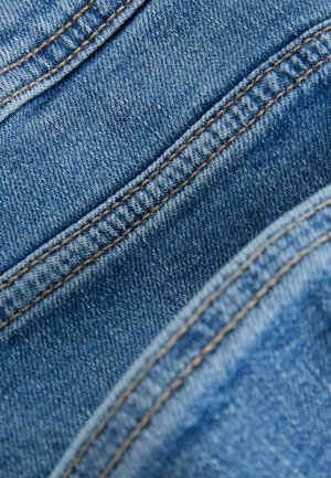 Denimová látka v odtieňoch modrej s viditeľným prešívaním v kontrastnej zlatej farbe, predstavujúca textúrovaný povrch a diagonálne záhyby.