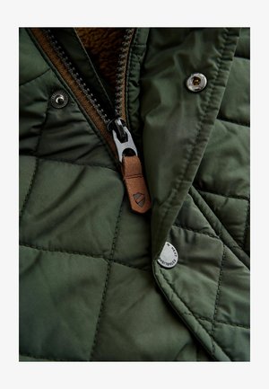 Padrėžta žalia striukė su ruda užtrauktuku, odiniu traukikliu ir sidabriniais sagčiais. Minkšta vidinė tekstūra su šiltu pamušalu.