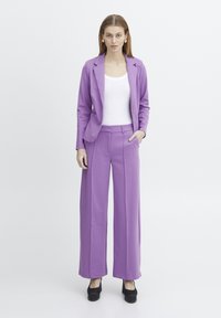 Ensemble composé d'un blazer violet et d'un pantalon évasé, fabriqué dans un tissu lisse. Le blazer a un col cranté ; le pantalon présente des poches latérales et une coupe ajustée.