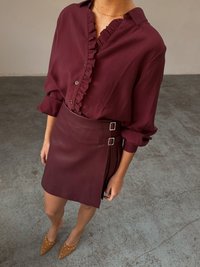 Burgundy blouse with ruffled collar and buttons, paired with a matching skirt featuring a side buckle. Tan pointed shoes with studs.