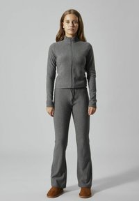 Veste zippée grise et pantalon évasé assorti en tissu doux et texturé. Le modèle porte des chaussures à enfiler marron.
