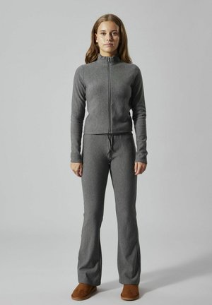 Grå hættejakke med lynlås og matchende flared bukser lavet af et blødt, tekstureret stof. Modellen bærer brune slip-on fodtøj.