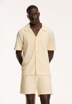 Light yellow, short-sleeve, button-up shirt and matching shorts made of textured waffle knit fabric. Simple design with a collar.