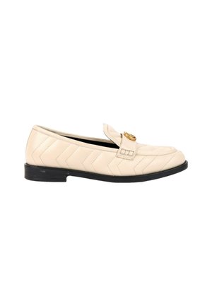 Beige læderloafer med chevron-quiltning, lav sort sål og guldfarvet rund spænde på toppen.