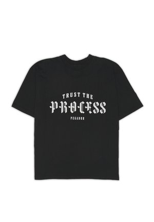 Musta lyhythihainen pyöreäkauluksinen t-paita, jossa valkoisella goottilaistyylisellä tekstillä lukee "Trust the Process" ja pienemmällä tekstillä "Pegador" alapuolella.