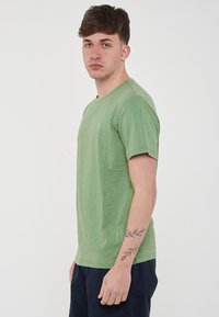 T-shirt a maniche corte, con collo rotondo, di colore verde chiaro, realizzato in materiale morbido. Presenta un piccolo logo sul petto e una vestibilità comoda.