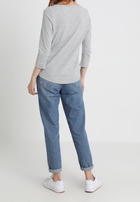 Grå topp med trekvartsärmar som bärs tillsammans med löst sittande blå jeans. Jeanserna är uppvikta vid fållarna och hon har på sig vita sneakers.