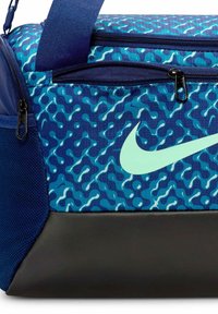 Nike sportinis krepšys su mėlynu raštuotu audiniu, turintis mėtos žalumos logotipą ir akcentus, juodą pagrindą bei kelis užtrauktukais uždaromus skyrius.