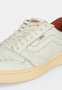 Λευκό δερμάτινο sneaker Vans με κρεμ σόλα, λευκά κορδόνια, διάτρητο σχέδιο στο πλευρό και καφέ εσωτερική επένδυση.
