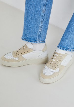 Fehér és bézs sneaker, perforált részletekkel, sima bőr felsőrésszel és vastag gumitalppal. Világoskék farmerrel párosítva.