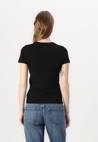 T-shirt noir à manches courtes avec un col rond, au design ajusté et à la texture lisse, associé à un jean taille haute bleu clair.
