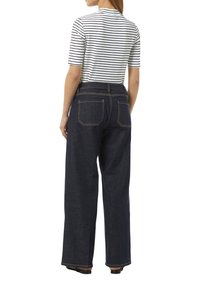 Gestreiftes Rippenshirt in Weiß und Marineblau, kombiniert mit hochtaillierten, dunklen Denim-Hosen mit weitem Bein, die über Gesäßtaschen und goldene Nähte verfügen.