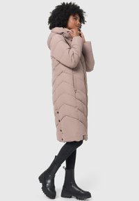 Puffer coat in soft beige with a hood, featuring chevron stitching, snap buttons on the hem, and side pockets, paired with black combat boots.
