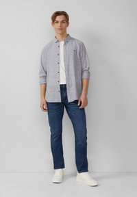 Zachtblauwe geblokte overhemd, witte ronde hals t-shirt, donkerblauwe jeans en witte sneakers. Ontspannen pasvorm, opgerolde mouwen, eenvoudig ontwerp.