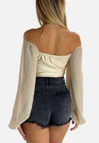 Cremfarbenes, schulterfreies Oberteil mit langen, transparenteren Ärmeln, kombiniert mit hoch sitzenden schwarzen Jeansshorts mit fransigem Saum und Gesäßtaschen.
