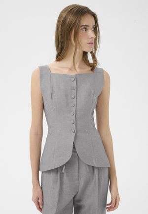 Kvinde iført en ærmeløs grå knaplukket top med firkantet halsudskæring og matchende løstsiddende bukser, der kigger mod højre.