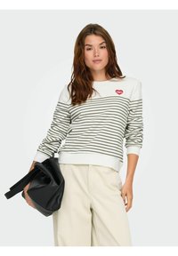 Sweter w paski w kolorze kremowym i oliwkowym z grafiką czerwonej szminki, okrągłym dekoltem, ściągaczami oraz luźnym krojem, w połączeniu z czarną torebką.