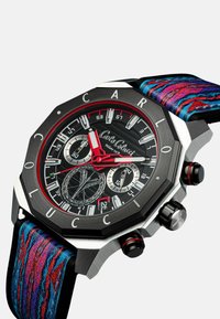 Orologio ottagonale con quadrante nero e accenti rossi, cassa in acciaio inossidabile e cinturino in tessuto multicolore con motivi blu e rossi.