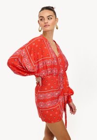 Vestido rojo con un estampado, escote en V, mangas oversize y ajuste en la cintura con lazo. Presenta diseños de paisley y flores en acentos contrastantes de blanco y rosa.