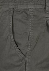 Gros plan sur un pantalon en tissu gris montrant une poche avant avec des coutures visibles et la texture du tissu.