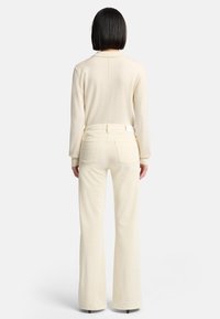 Kremfarvet striktrøje med en lige søm på ryggen, kombineret med lyse flared bukser med en ensartet tekstur og baglommer.