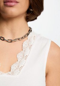 Top sin mangas blanco con textura acanalada y un cuello con borde de encaje, complementado con un collar de cadena plateada con eslabones ovalados.