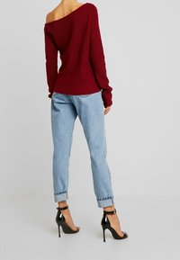 Maglione a maniche scese color bordeaux abbinato a jeans in denim light blue, con una vestibilità comoda e orli arrotolati, e sandali neri con tacco alto.